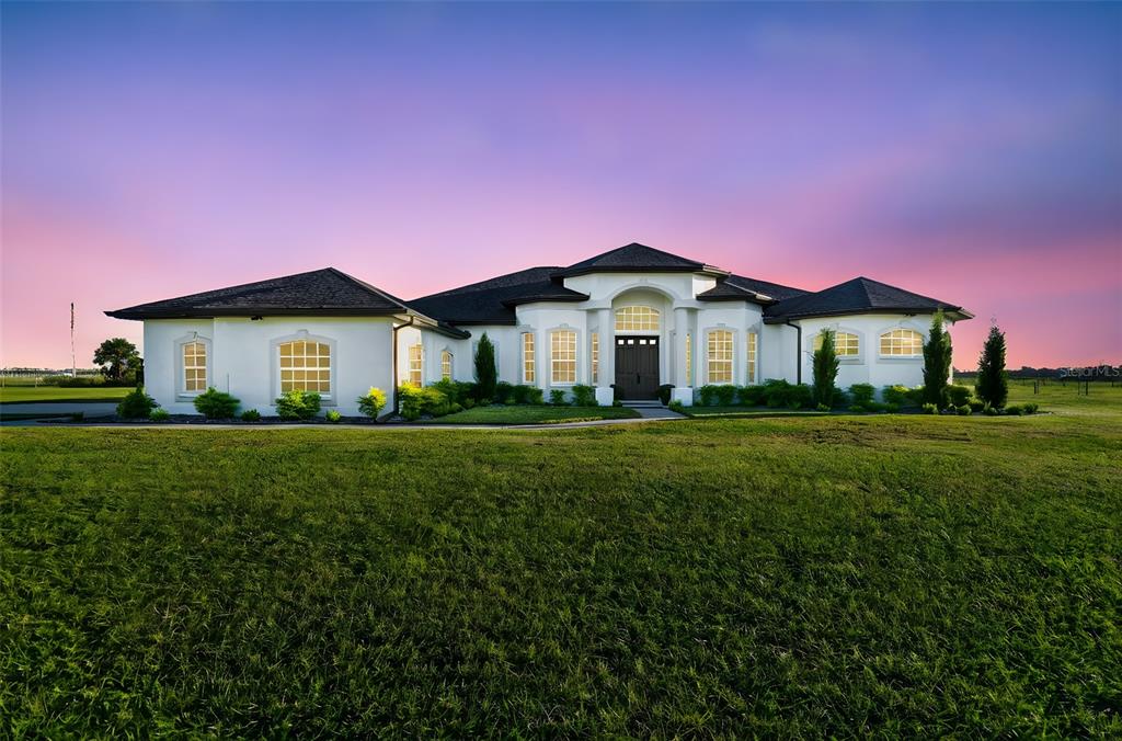 A single-story white house with a dark roof sits on a large, grassy lawn — 15639 SETH COUNTRY LANE, WIMAUMA, FL