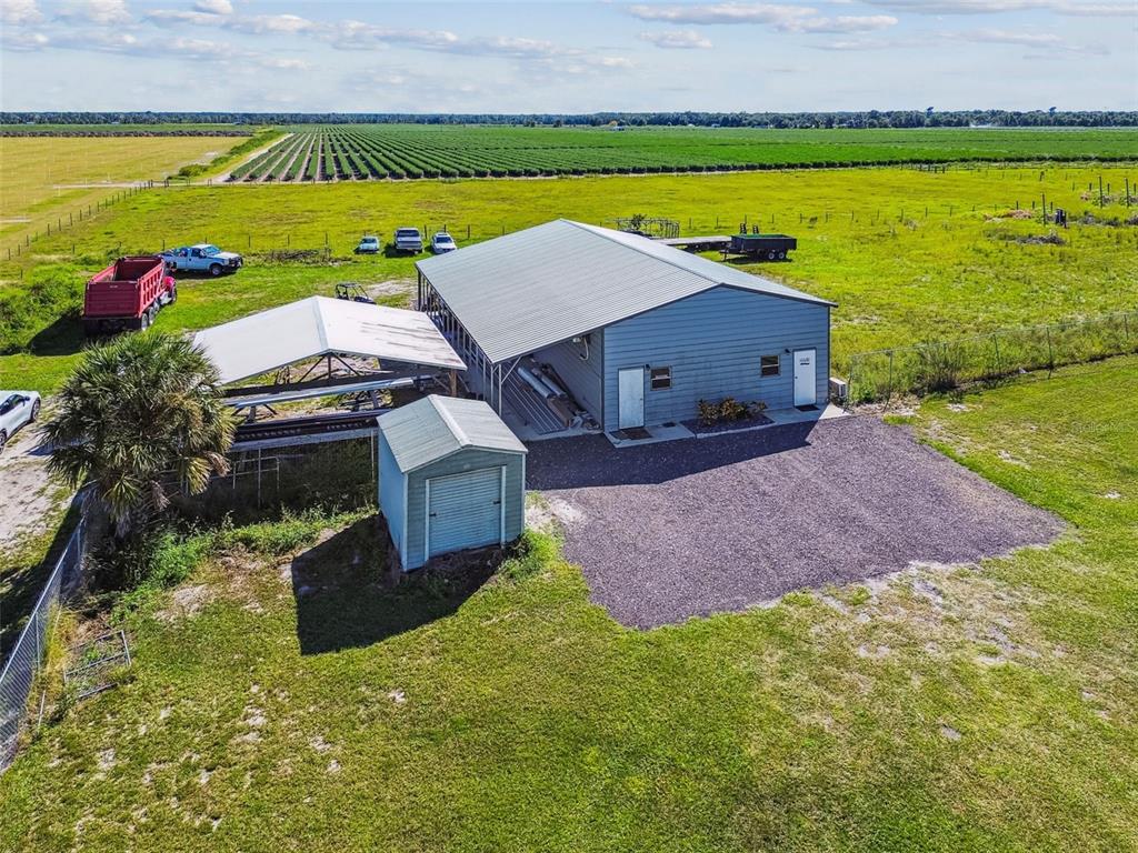 An aerial view shows a metal workshop building with an attached carport and small shed — 15639 SETH COUNTRY LANE, WIMAUMA, FL