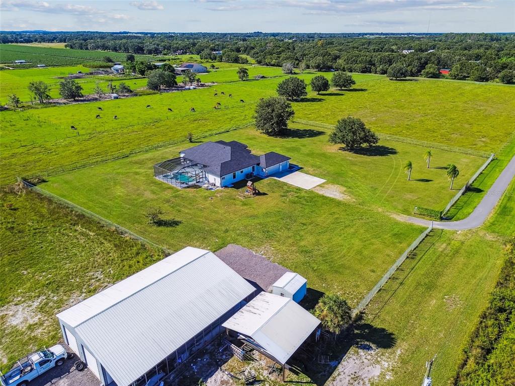 An aerial view shows a house with a pool, a large workshop, and surrounding pastures — 15639 SETH COUNTRY LANE, WIMAUMA, FL
