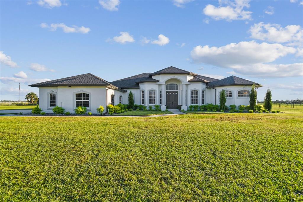 A single-story white stucco house with a dark shingled roof sits on a grassy lot — 15639 SETH COUNTRY LANE, WIMAUMA, FL
