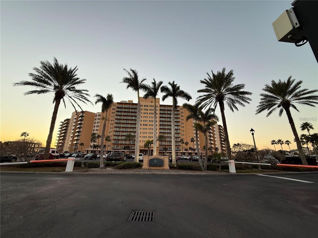 A multi-story tan apartment building stands behind a parking lot with several palm trees — 880 MANDALAY AVENUE UNIT C410, CLEARWATER, FL