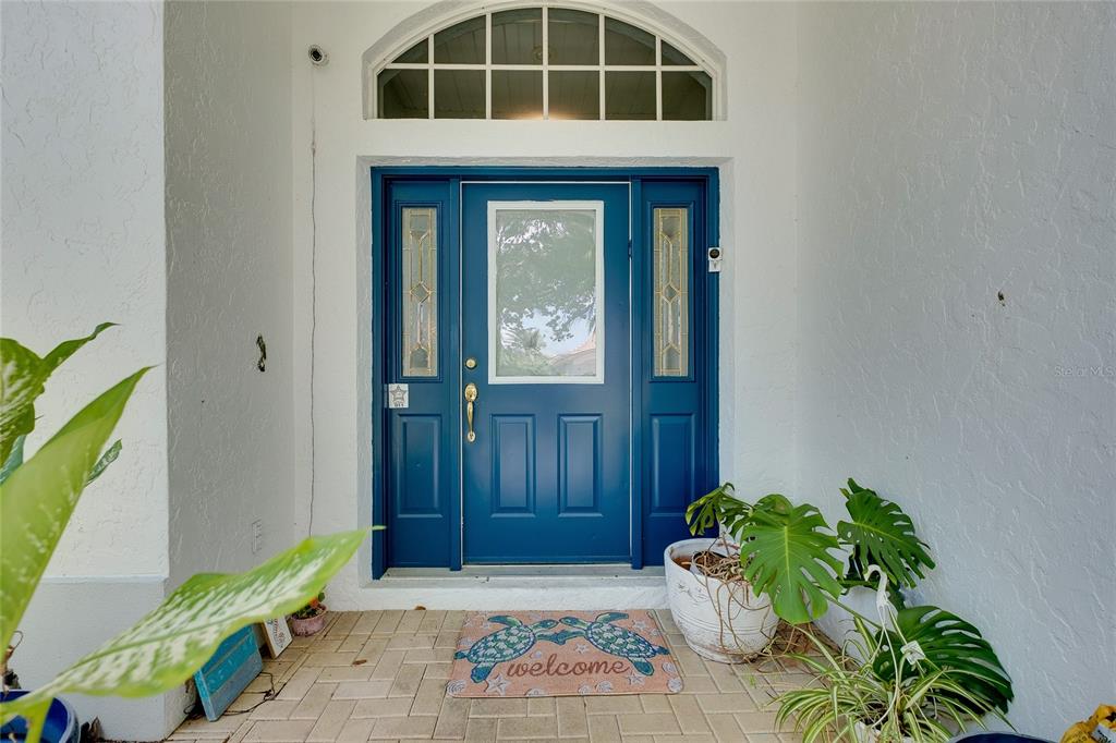A blue front door with a glass insert and sidelights sits on a paved porch — 360 CEDARBROOK COURT, VENICE, FL