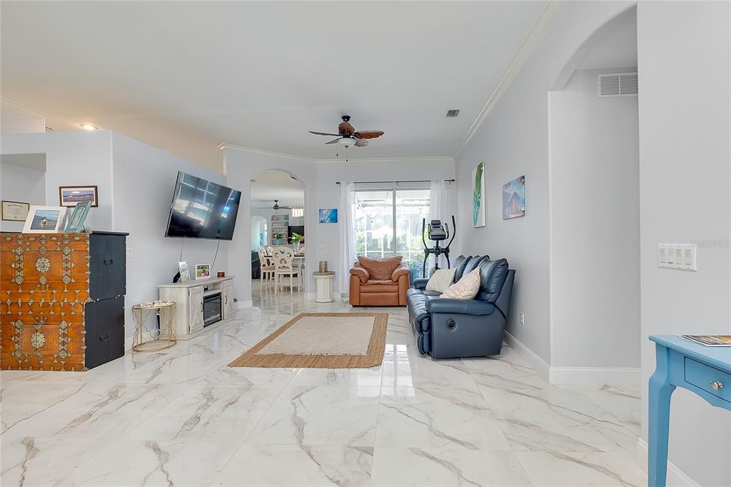 A living room features white marble-look tile floors, a blue sofa, and a television console — 360 CEDARBROOK COURT, VENICE, FL