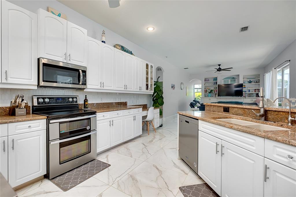 A white kitchen features granite countertops, stainless steel appliances, and light-colored marble-look tile flooring — 360 CEDARBROOK COURT, VENICE, FL