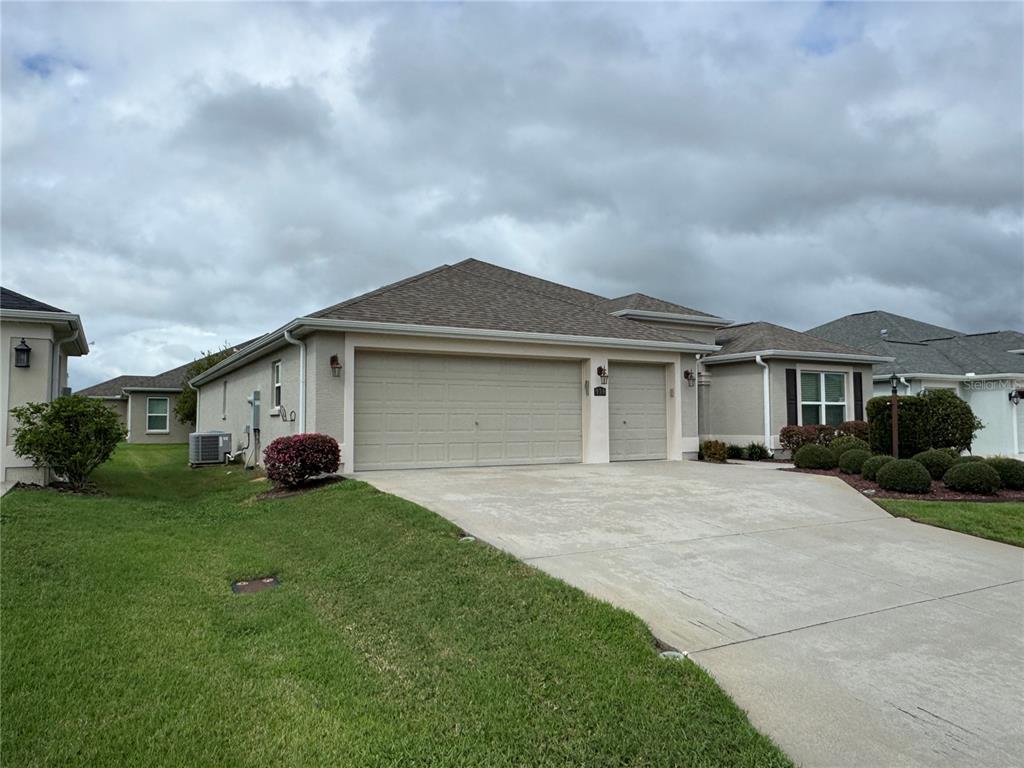 A beige house with a three-car garage and a concrete driveway under a cloudy sky — 939 KOLLER COURT, THE VILLAGES, FL