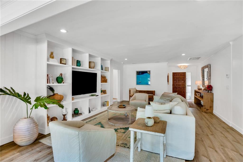 A bright living room features white built-in shelving, a television, and light wood flooring — VERO BEACH, FL