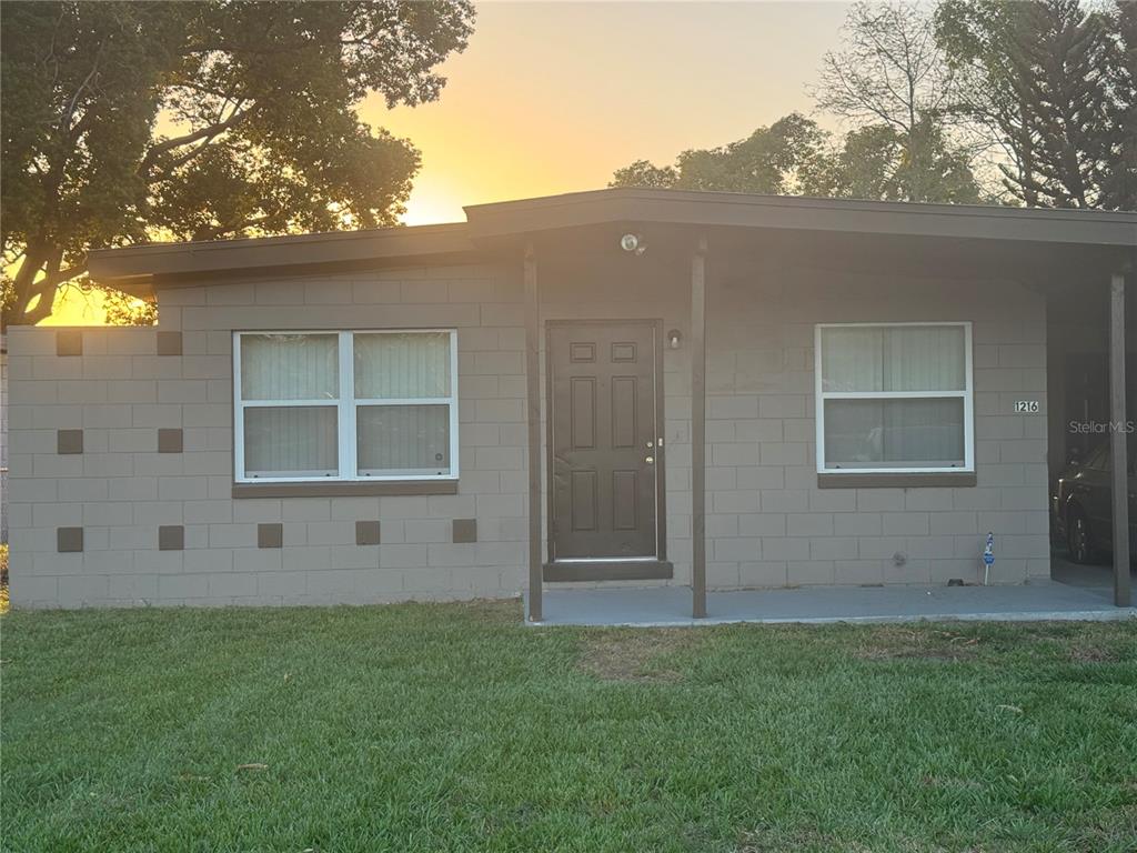 A single-story house with a gray concrete block exterior, a dark door, and a carport — 1216 LAWNE BOULEVARD, ORLANDO, FL