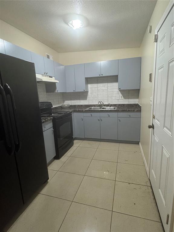 A kitchen features light blue cabinets, dark countertops, a black refrigerator, and tiled flooring — 1216 LAWNE BOULEVARD, ORLANDO, FL