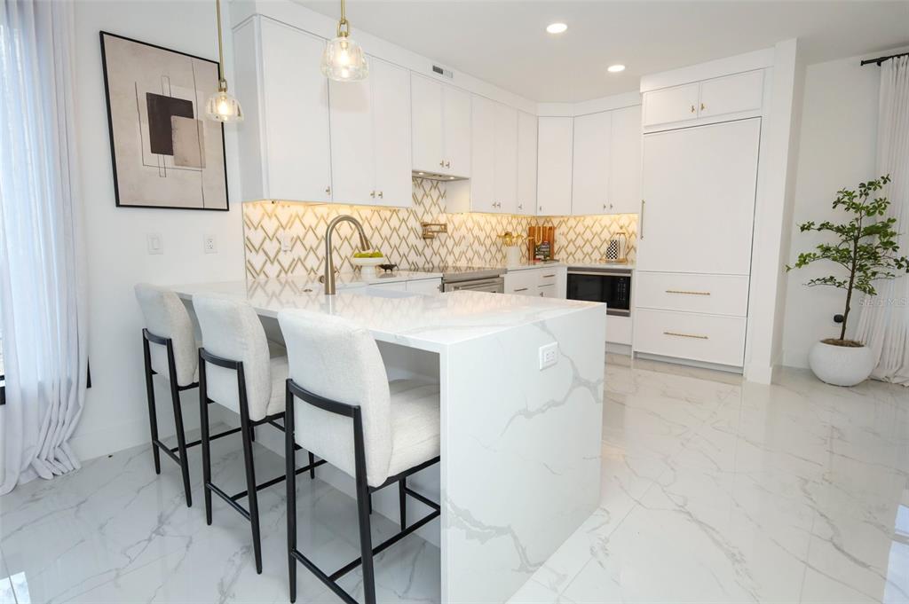 A modern kitchen features white cabinetry, a marble-topped island with bar stools, and patterned backsplash — 2360 OCEAN SHORE BOULEVARD UNIT 27, ORMOND BEACH, FL