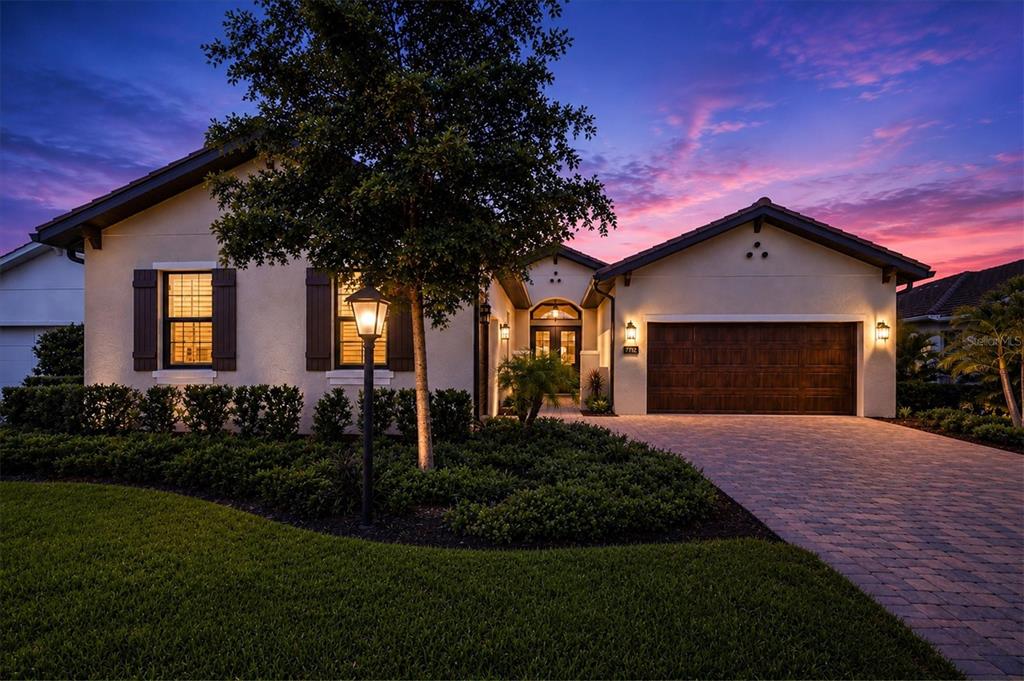 A single-story house with a paved driveway, dark wood garage door, and sunset sky — 7712 SANDHILL LAKE DRIVE, SARASOTA, FL