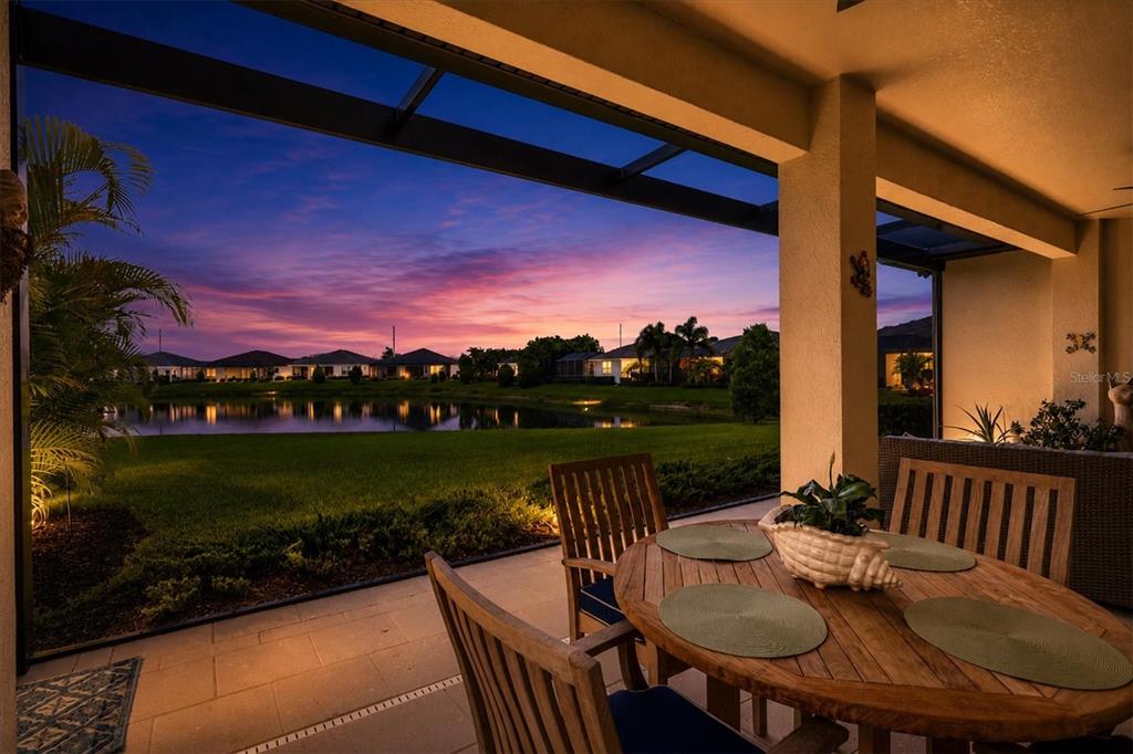 A covered patio with a wooden dining set overlooks a lake at sunset — 7712 SANDHILL LAKE DRIVE, SARASOTA, FL