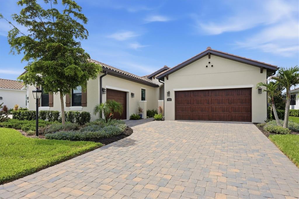A single-story house with a paved driveway, two garage doors, and a landscaped front yard — 7712 SANDHILL LAKE DRIVE, SARASOTA, FL