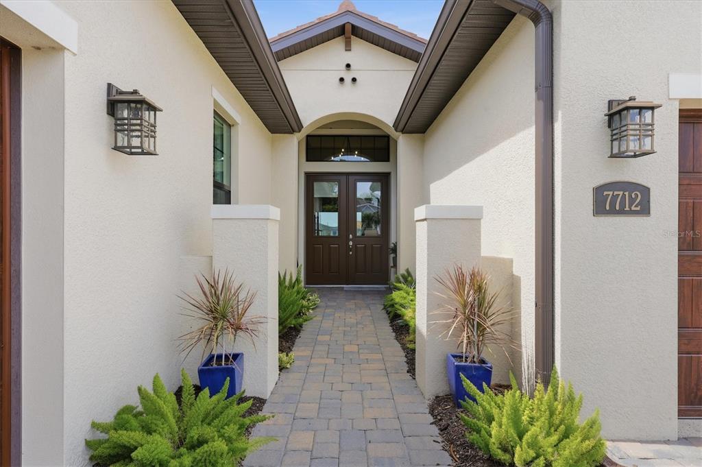 A paved walkway leads to the double front doors of a stucco house entrance — 7712 SANDHILL LAKE DRIVE, SARASOTA, FL