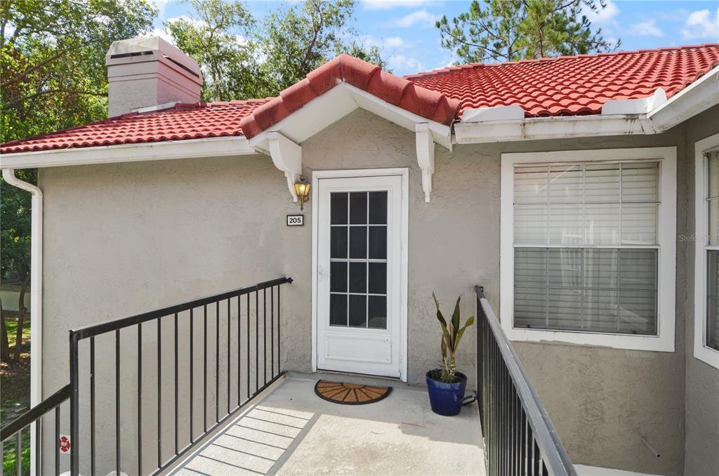 An exterior view of a building entrance with a red tile roof and black railings — 955 NORTHERN DANCER WAY UNIT 205, CASSELBERRY, FL