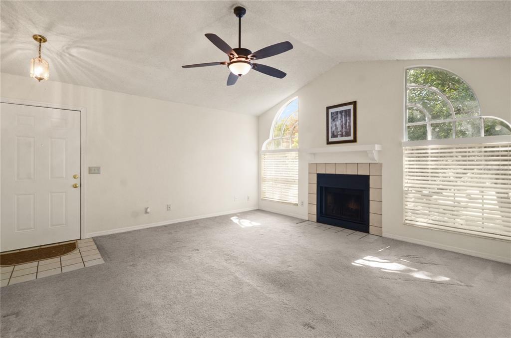 A living room with gray carpet, a fireplace, a ceiling fan, and arched windows — 955 NORTHERN DANCER WAY UNIT 205, CASSELBERRY, FL