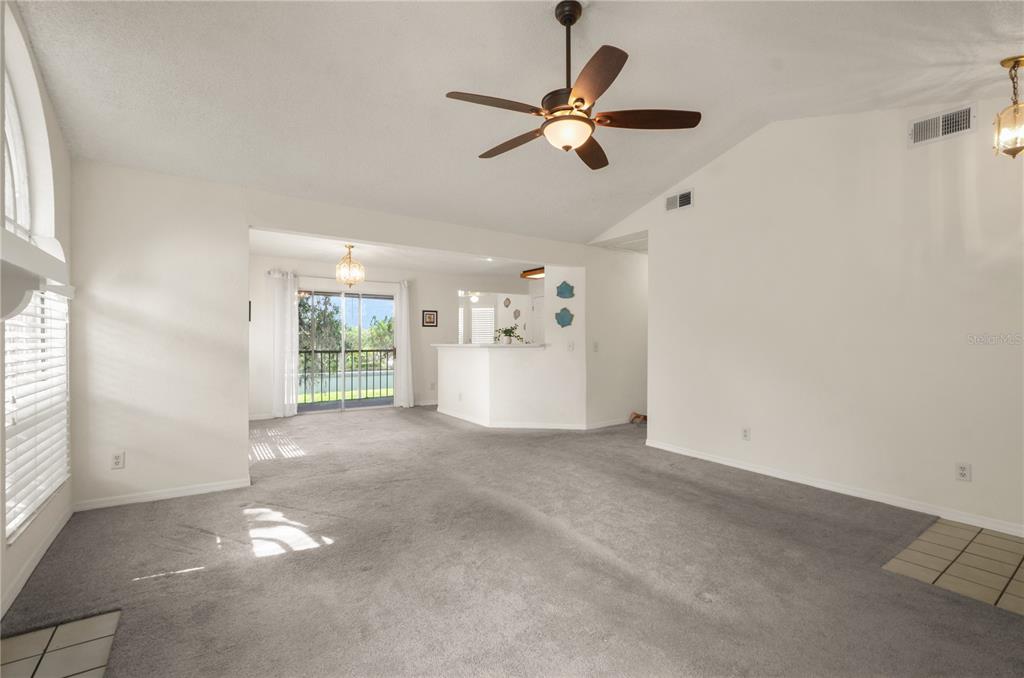 A spacious living room with gray carpet, a ceiling fan, and a view of a patio — 955 NORTHERN DANCER WAY UNIT 205, CASSELBERRY, FL