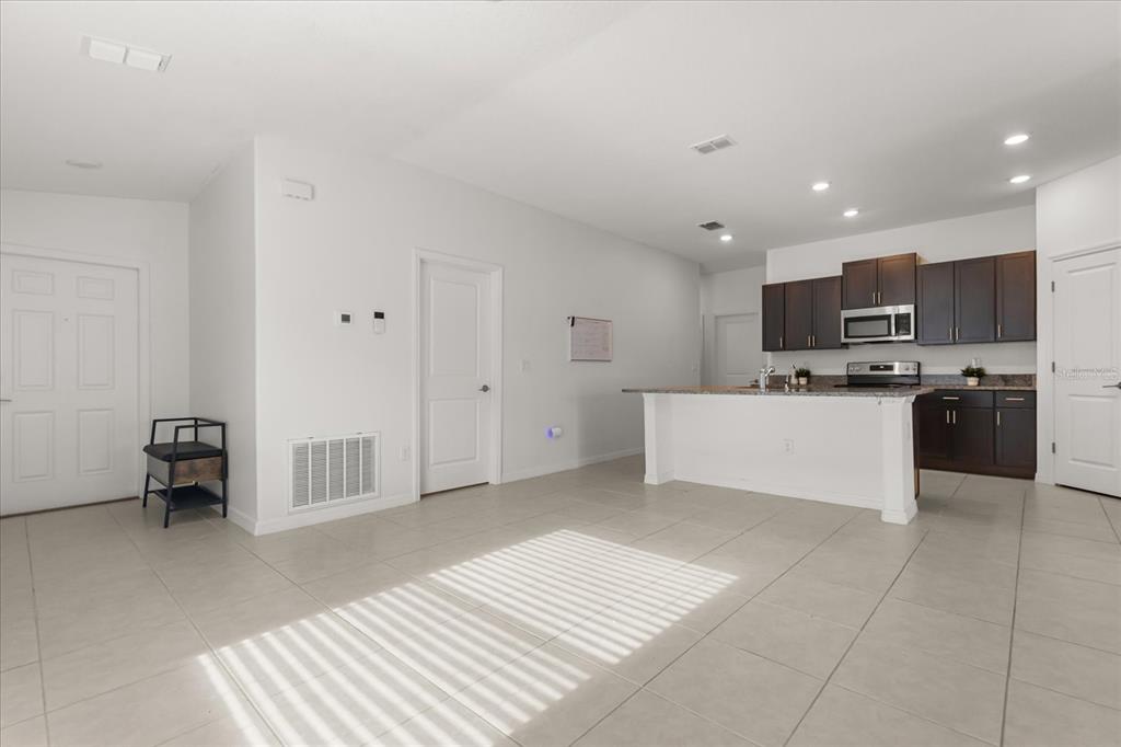 An open-concept living area features light tile flooring, white walls, and a kitchen with dark cabinets — 2674 RED EGRET DRIVE, BARTOW, FL
