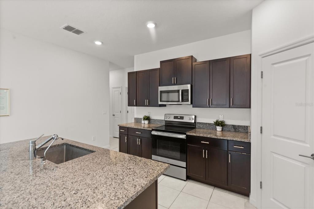 A kitchen features dark wood cabinets, granite countertops, stainless steel appliances, and a center island — 2674 RED EGRET DRIVE, BARTOW, FL
