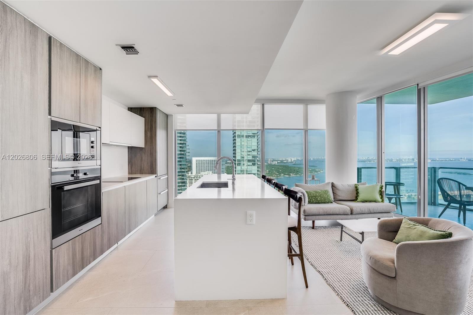 A modern kitchen and living area features a white island, wood cabinetry, and floor-to-ceiling windows — 2900 NE 7th Ave # 3702, Miami FL 33137, MIAMI, FL