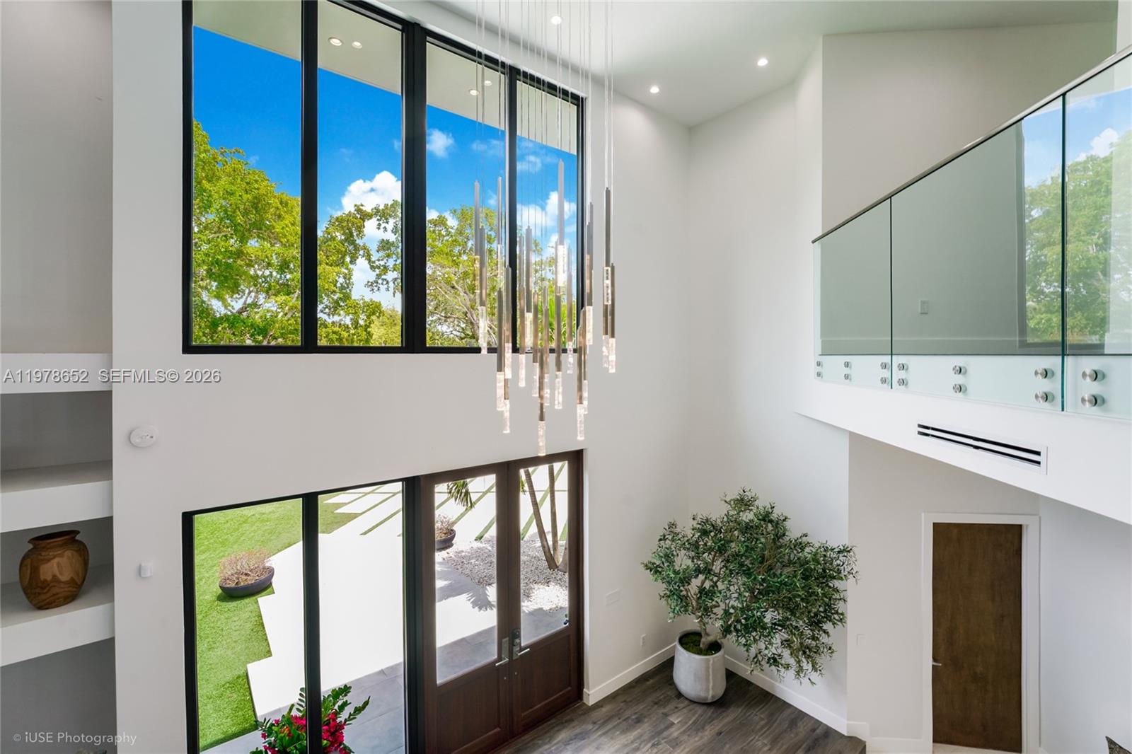A two-story foyer features a tall chandelier, floor-to-ceiling windows, and a glass-railed balcony — 56 Samana Dr, Miami FL 33133, MIAMI, FL