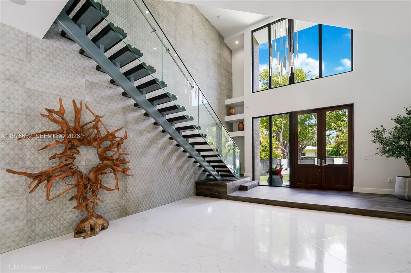 A modern foyer features a floating staircase, a large driftwood sculpture, and floor-to-ceiling windows — 56 Samana Dr, Miami FL 33133, MIAMI, FL