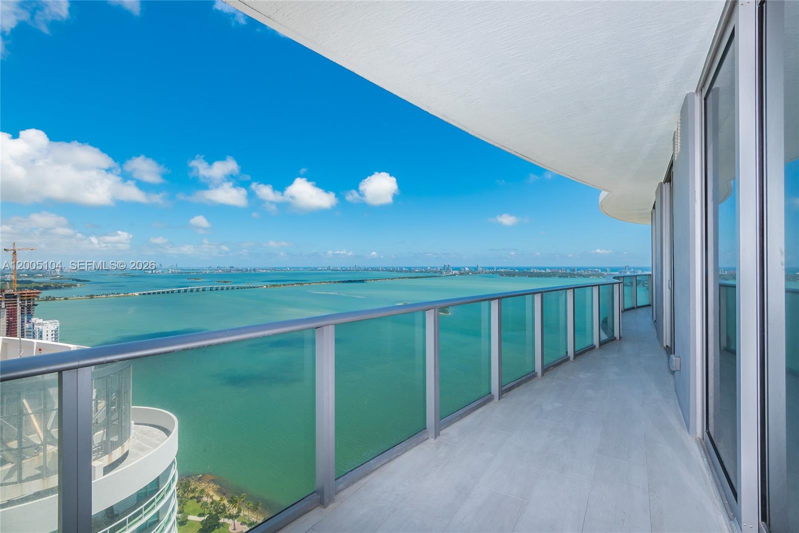 A high-rise balcony features a glass railing overlooking a bay with a distant bridge — 488 NE 18th St # 4515, Miami FL 33132, MIAMI, FL