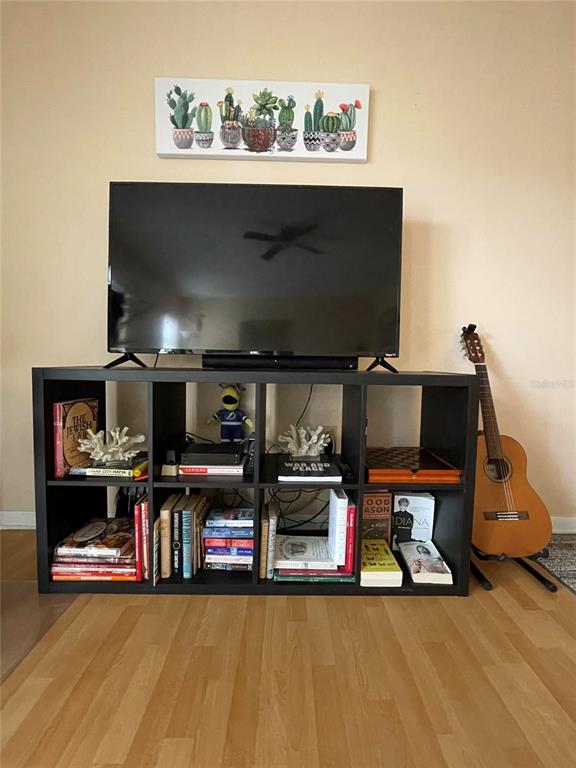 A black cube storage unit holds books and decor beneath a television and wall art — 239 S MCMULLEN BOOTH ROAD UNIT 38, CLEARWATER, FL
