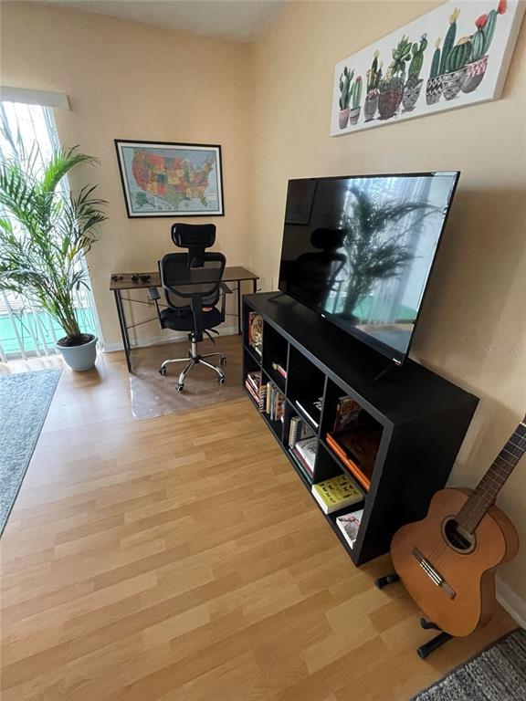 A living room features a television on a black storage unit, a desk, and a guitar — 239 S MCMULLEN BOOTH ROAD UNIT 38, CLEARWATER, FL