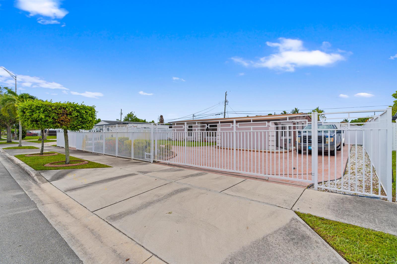 A single-story house with a white fence and a paved driveway sits behind a gate — 6160 W 14th Avenue, Hialeah FL 33012, HIALEAH, FL