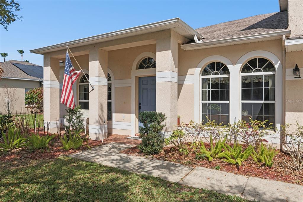 The exterior of a beige house features a covered entryway, a blue door, and arched windows — 1209 CASTLEPORT ROAD, WINTER GARDEN, FL