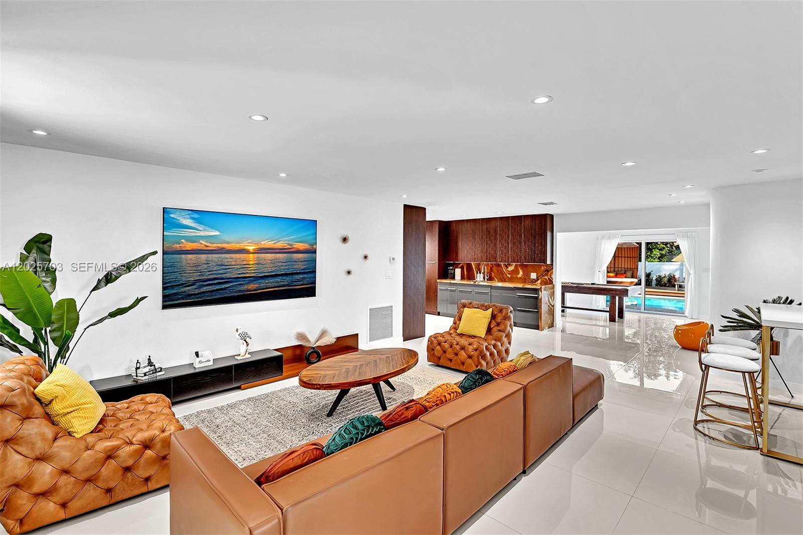 A modern living room features a large television, leather seating, and an open kitchen area — 5005 Johnson St, Hollywood FL 33021, HOLLYWOOD, FL