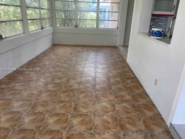 An empty room features brown patterned tile flooring and large windows overlooking greenery — 4501 Mainland Dr, Tamarac FL 33319, TAMARAC, FL