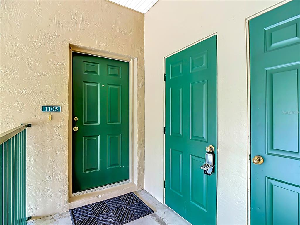 Three green doors are set into a beige stucco wall on an outdoor walkway — 1105 EAGLE POND DRIVE UNIT 1105, WINTER HAVEN, FL