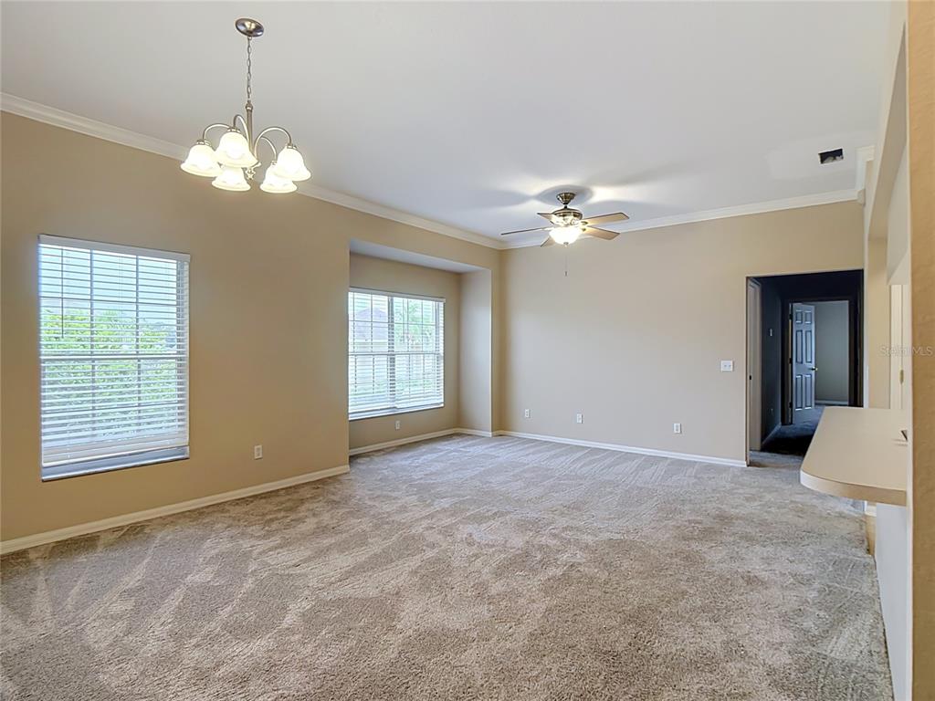 An empty living room features beige walls, carpeted flooring, a ceiling fan, and a chandelier — 1105 EAGLE POND DRIVE UNIT 1105, WINTER HAVEN, FL