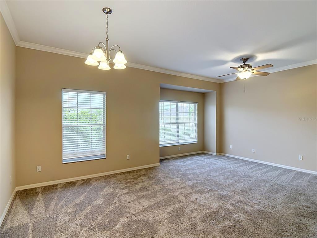 An empty room with beige walls, gray carpet, a ceiling fan, and a chandelier — 1105 EAGLE POND DRIVE UNIT 1105, WINTER HAVEN, FL