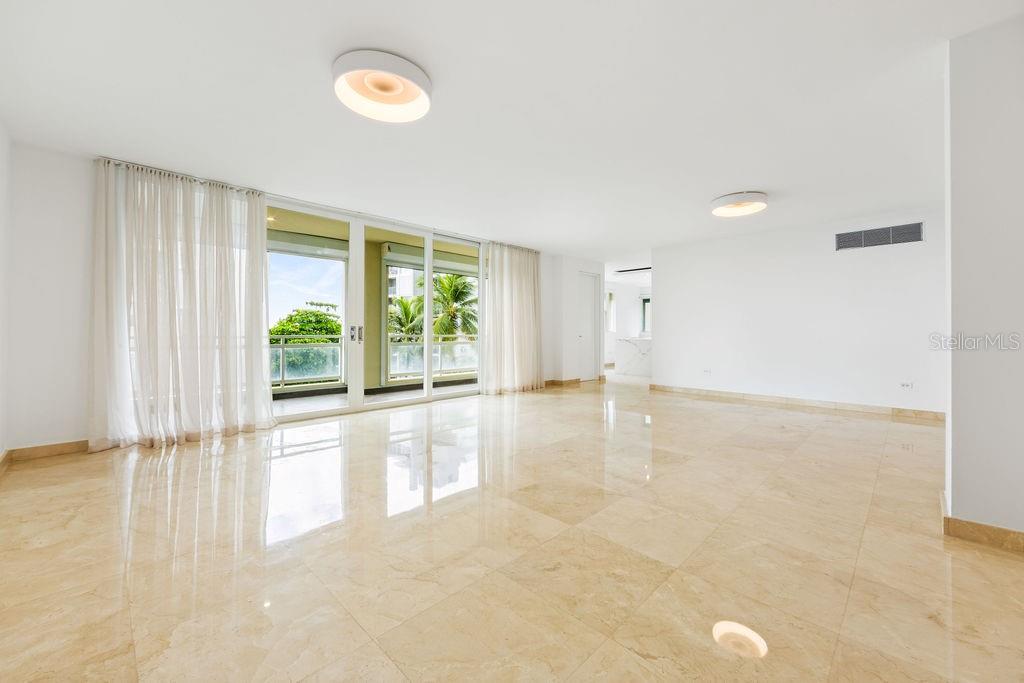 An empty living room features polished beige tile floors, white walls, and large sliding glass doors — 20 CARRION COURT UNIT 401, SAN JUAN, PR