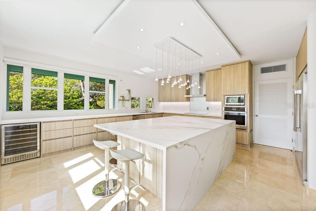 A modern kitchen features a large marble waterfall island, light wood cabinetry, and floor-to-ceiling windows — 20 CARRION COURT UNIT 401, SAN JUAN, PR
