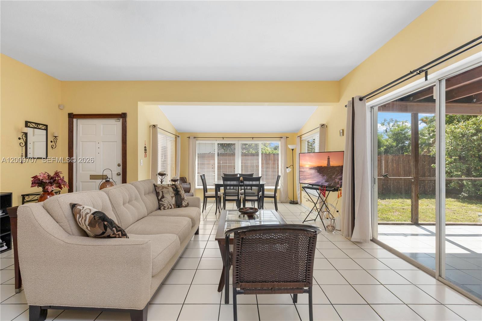 A living room with tile floors, a beige sofa, and a dining area near windows — 906 NE 5th St, Hallandale Beach FL 33009, HALLANDALE BEACH, FL