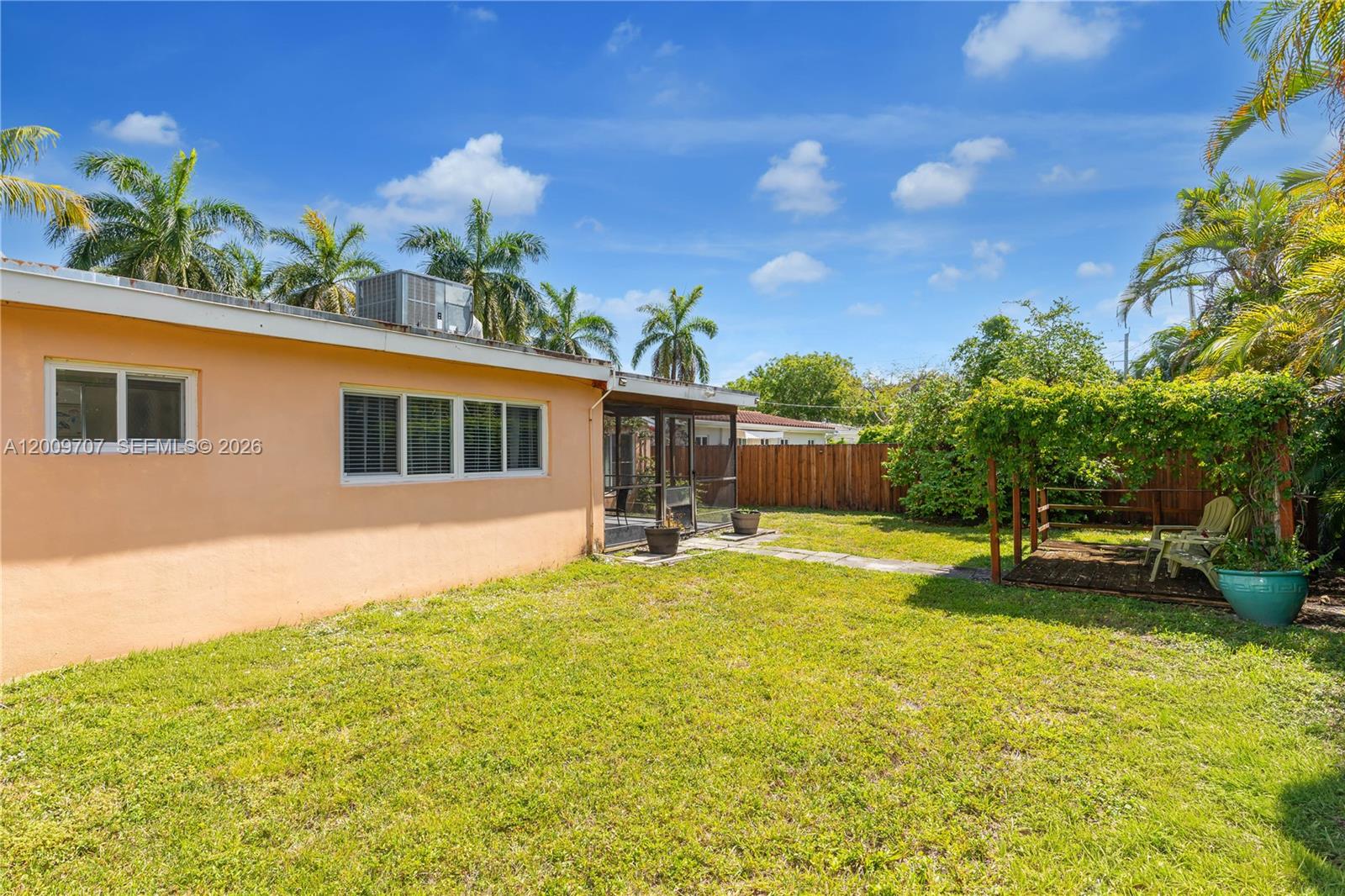 The backyard features a peach-colored house, a screened-in patio, and a wooden pergola — 906 NE 5th St, Hallandale Beach FL 33009, HALLANDALE BEACH, FL