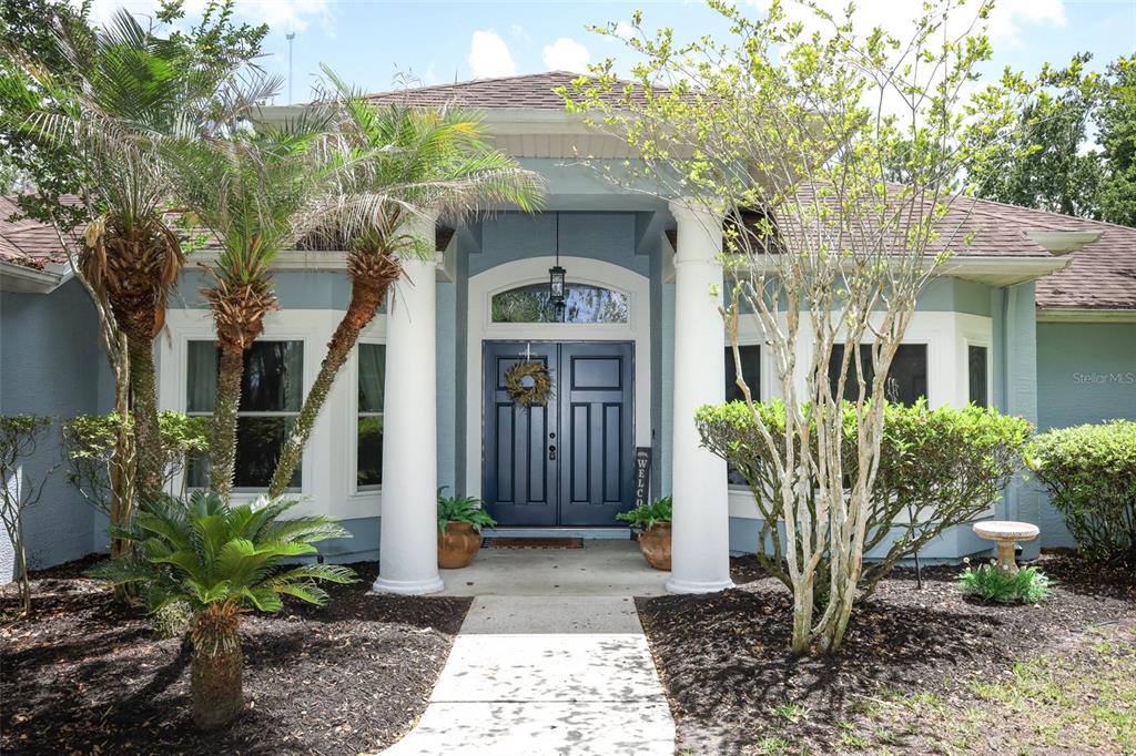 The front exterior of a house features a blue double door, white columns, and landscaping — 2461 WASSUM TRAIL, OVIEDO, FL