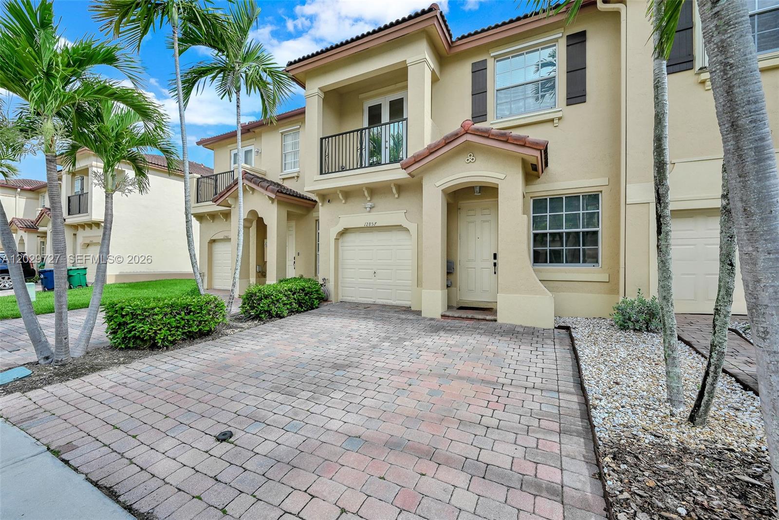 A two-story townhouse with a paved driveway, a single-car garage, and a small balcony — 12857 SW 134th St, Miami FL 33186, MIAMI, FL