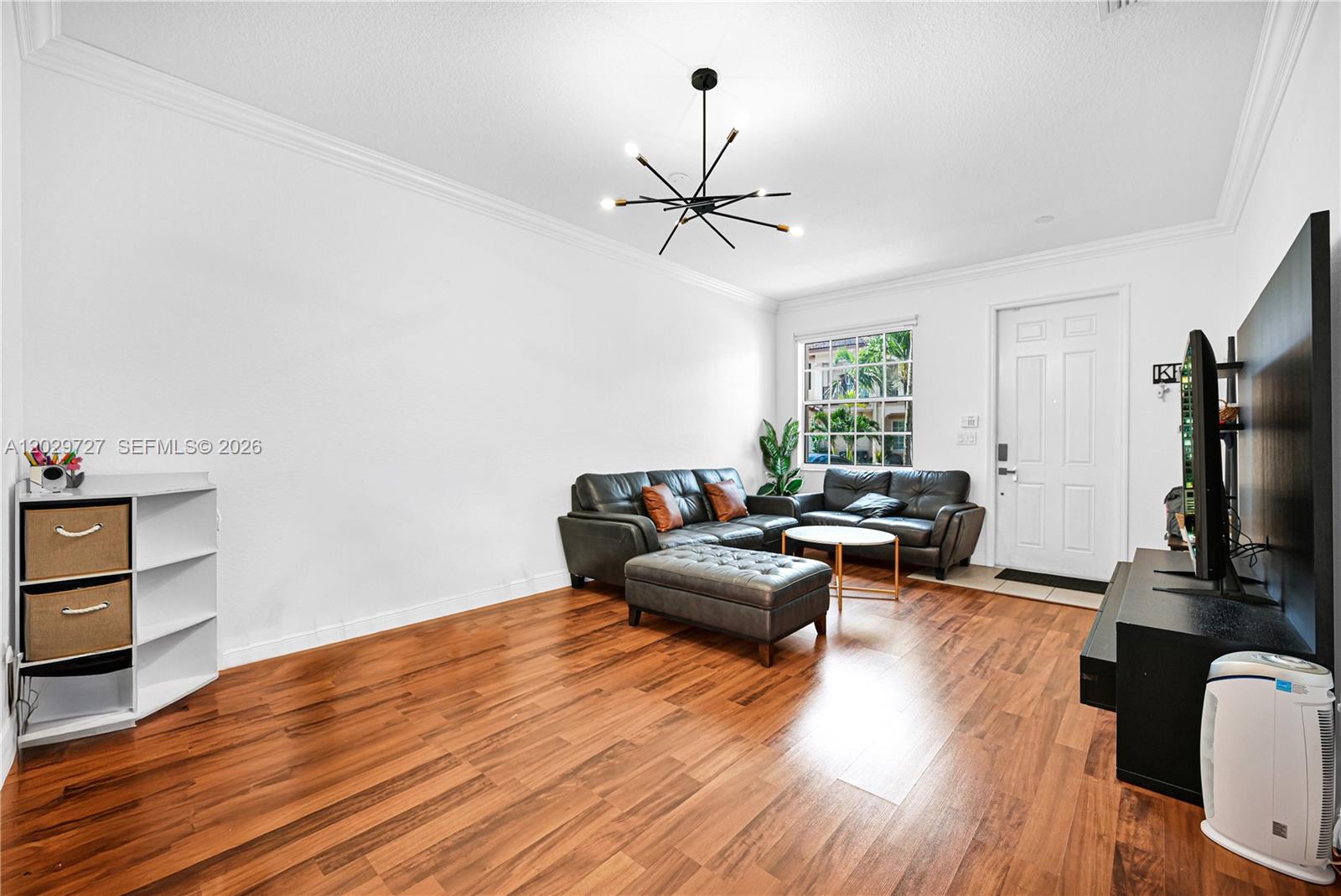 A living room features dark leather seating, wood-look flooring, and a modern sputnik chandelier — 12857 SW 134th St, Miami FL 33186, MIAMI, FL