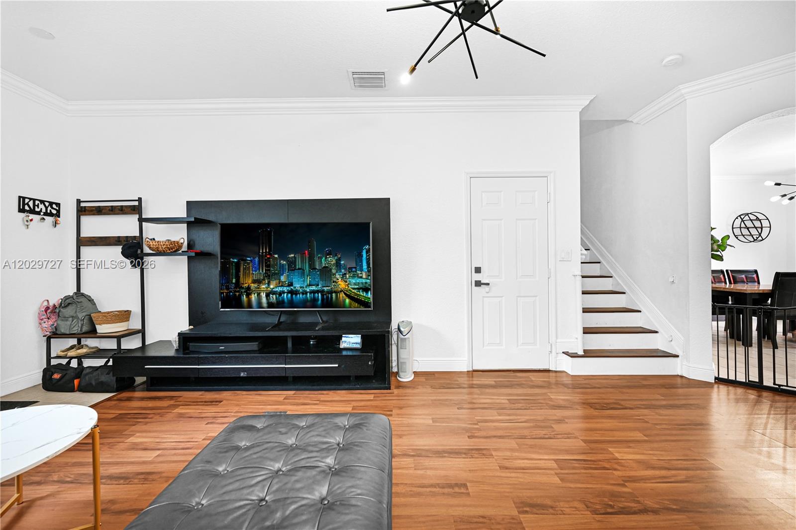A living room features a wall-mounted television, dark wood flooring, and a staircase — 12857 SW 134th St, Miami FL 33186, MIAMI, FL