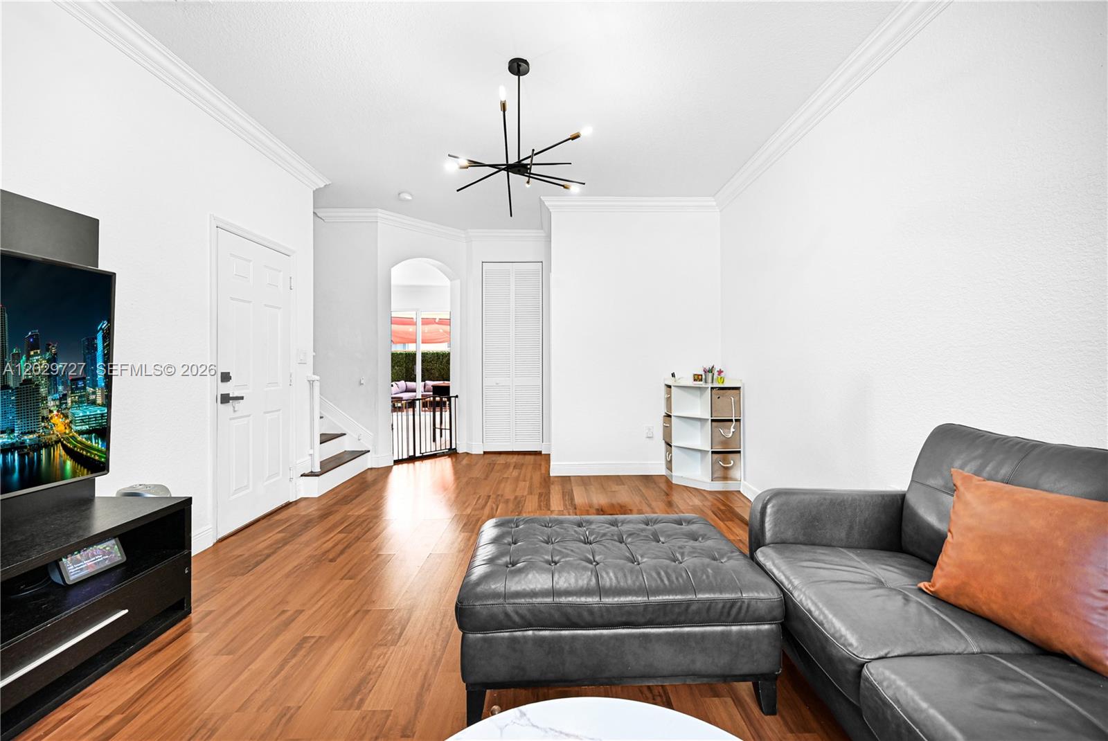 A living room features hardwood floors, a grey leather sofa, and a modern chandelier — 12857 SW 134th St, Miami FL 33186, MIAMI, FL