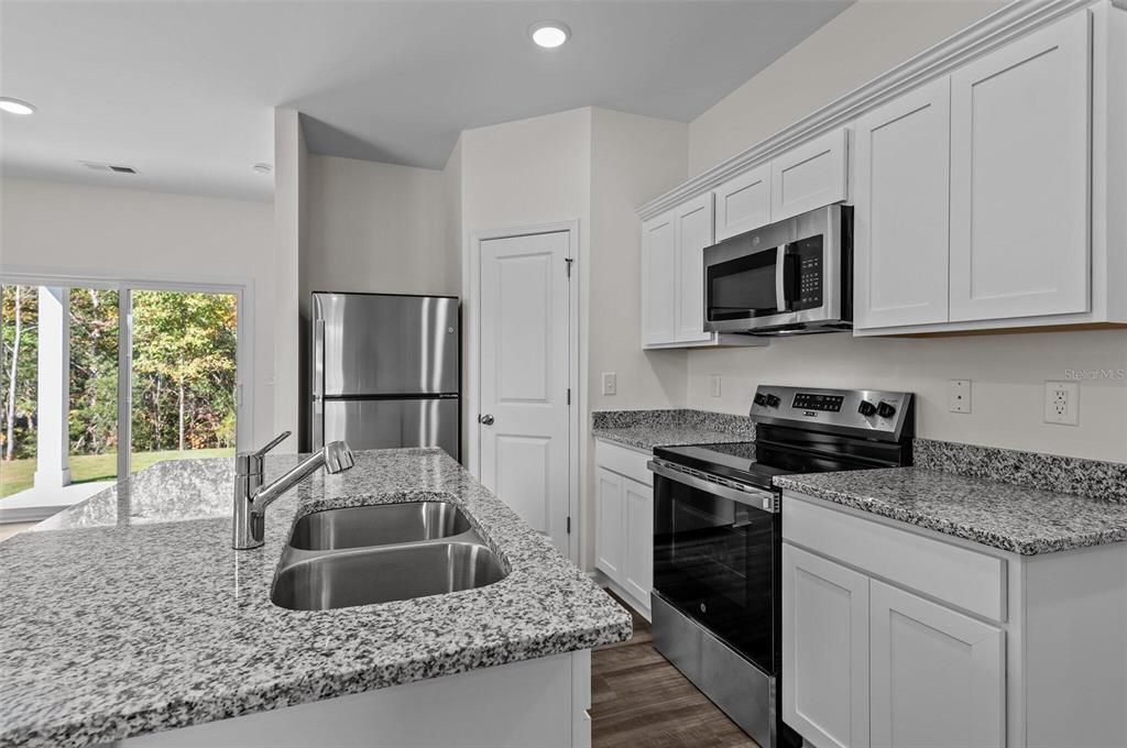 A kitchen features white cabinets, granite countertops, stainless steel appliances, and a central island sink — 14626 ITALY AVENUE, DADE CITY, FL