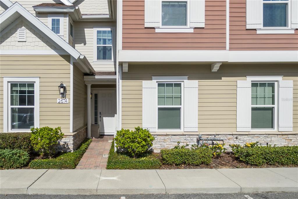 A two-story townhouse exterior features tan siding, a white front door, and a stone base — 2614 SUNRISE SHORES DRIVE, KISSIMMEE, FL