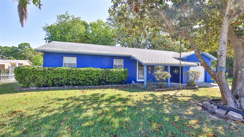 A single-story blue house with a covered porch and a large hedge in the front — 1915 UMBRELLA TREE DRIVE, EDGEWATER, FL