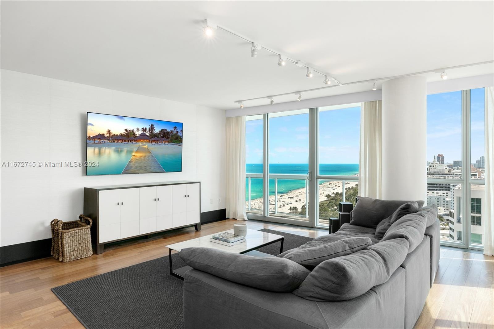 A living room features a large television, a grey sofa, and floor-to-ceiling oceanfront windows — 101 20th St # 2706, Miami Beach FL 33139, MIAMI BEACH, FL