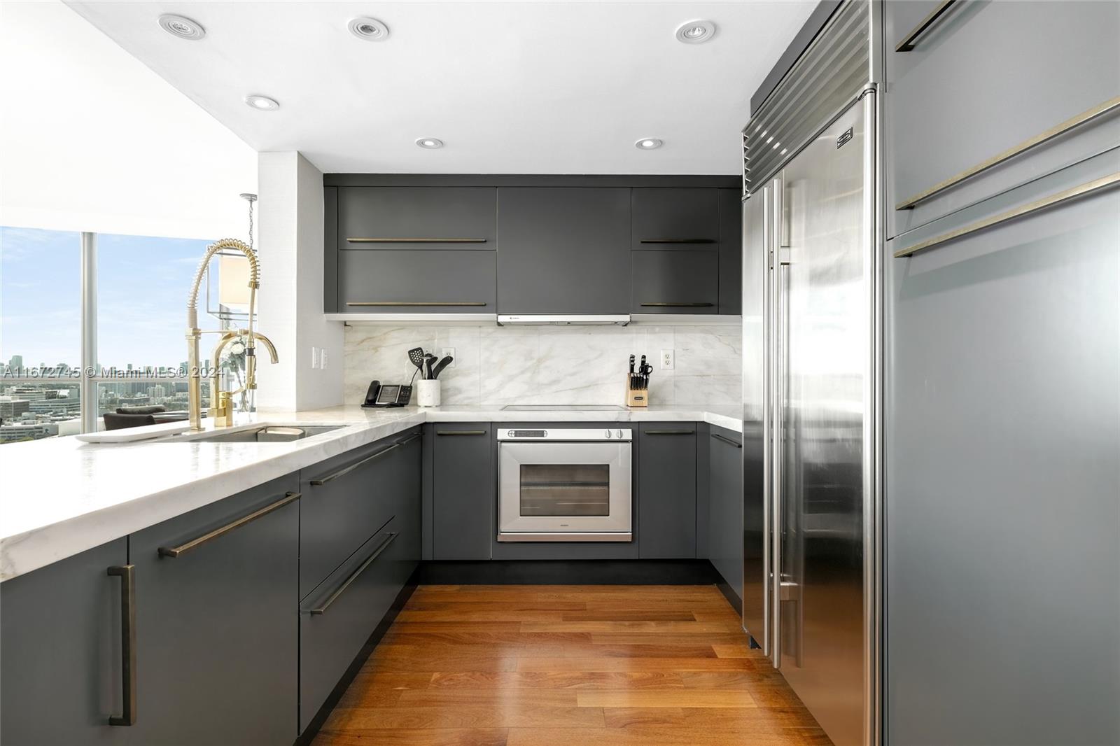 A modern kitchen features dark gray cabinetry, stainless steel appliances, and a marble countertop — 101 20th St # 2706, Miami Beach FL 33139, MIAMI BEACH, FL