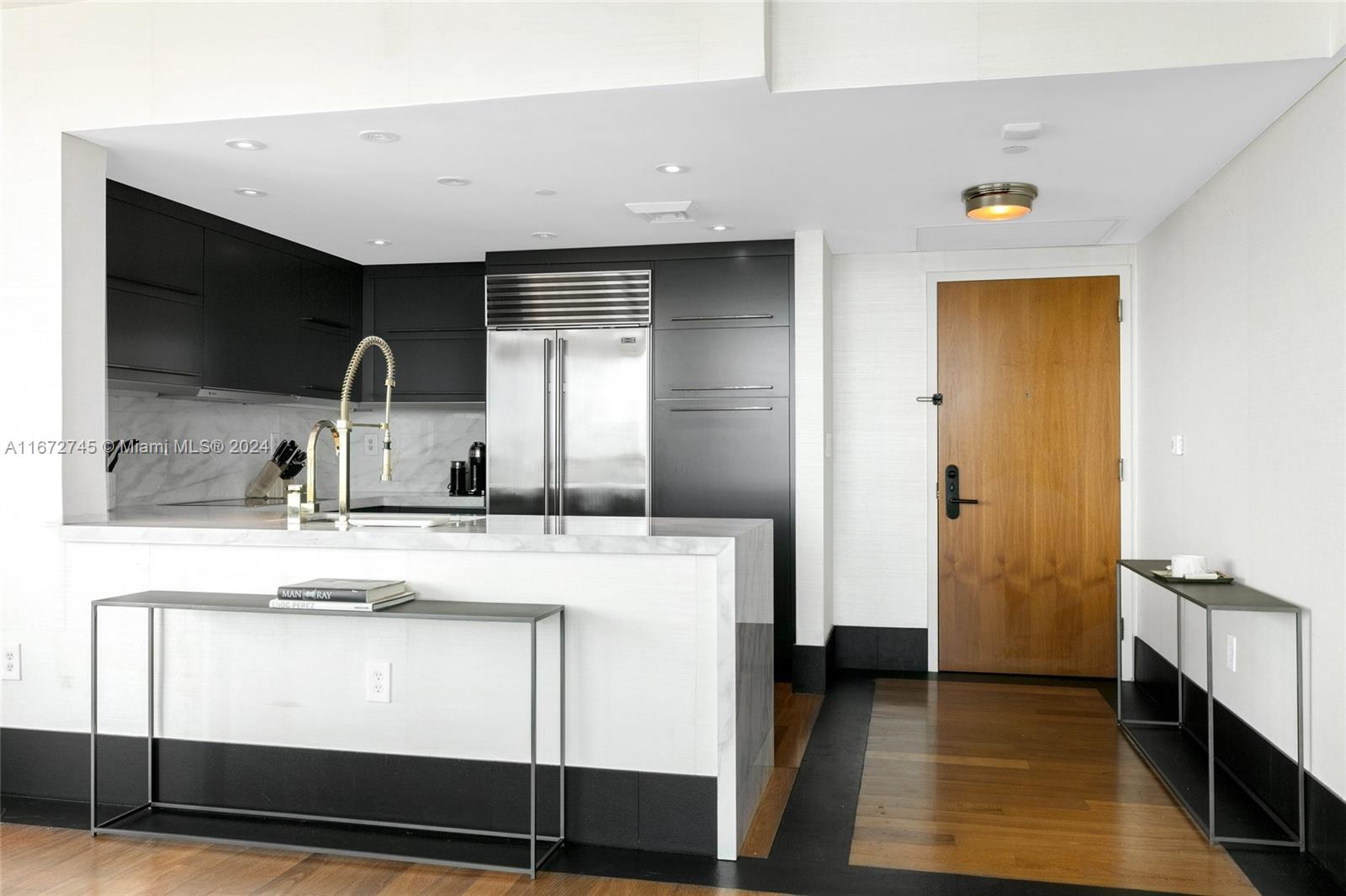 A modern kitchen features black cabinetry, a marble island, and a wooden entry door — 101 20th St # 2706, Miami Beach FL 33139, MIAMI BEACH, FL